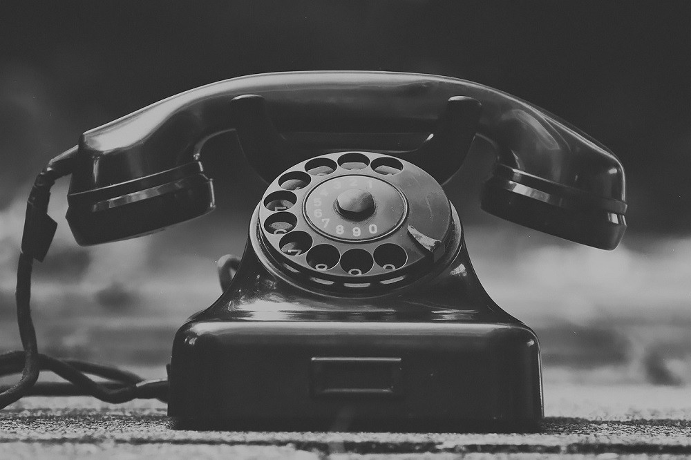A dusty black rotary phone sits on a table
