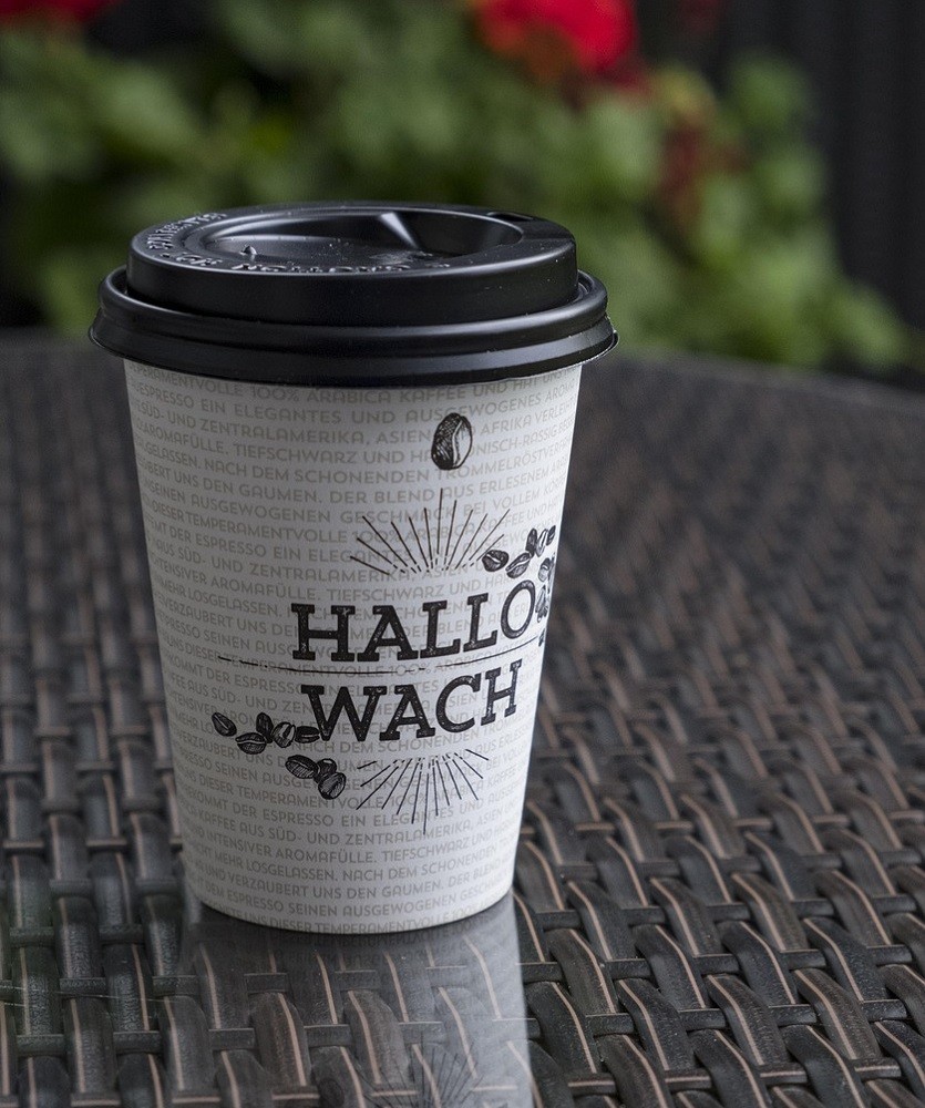 A white to-go paper coffee cup with a black plastic lid sits on a table