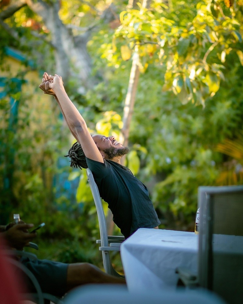 A man in a green tee shirt sits at a table with his arms outstretched. He is cheering