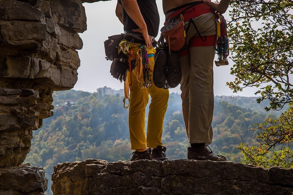 Two rock climbers stand at the summit of a sheer rock face