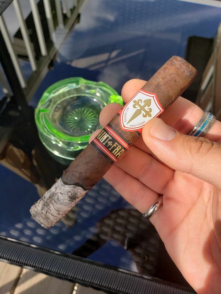 The All Saints Cigar by Saint Francis has about 2 inches of ash on it and shows a slightly wavy burn where the tobacco leaf meets the ash