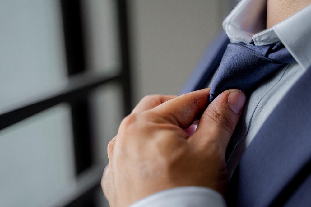 A businessman adjusts his blue tie. He is wearing a white dress shirt and a dark blue suit