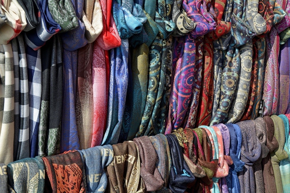 Multiple scarves are arranged on a rack. They range from solid colours to intricate patterns and come in a variety of colours