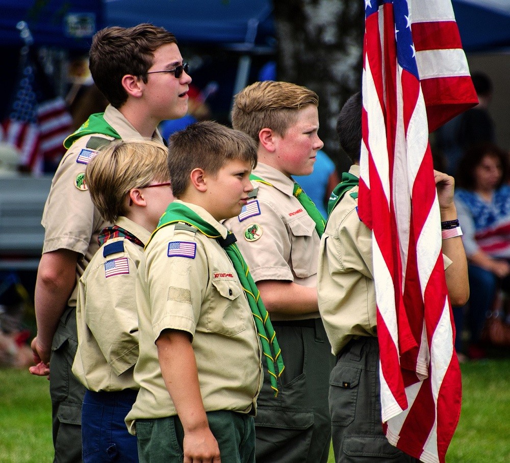 A group of scouts are standing at attention. They are wearing their formal scout attire complete with green neckerchiefs