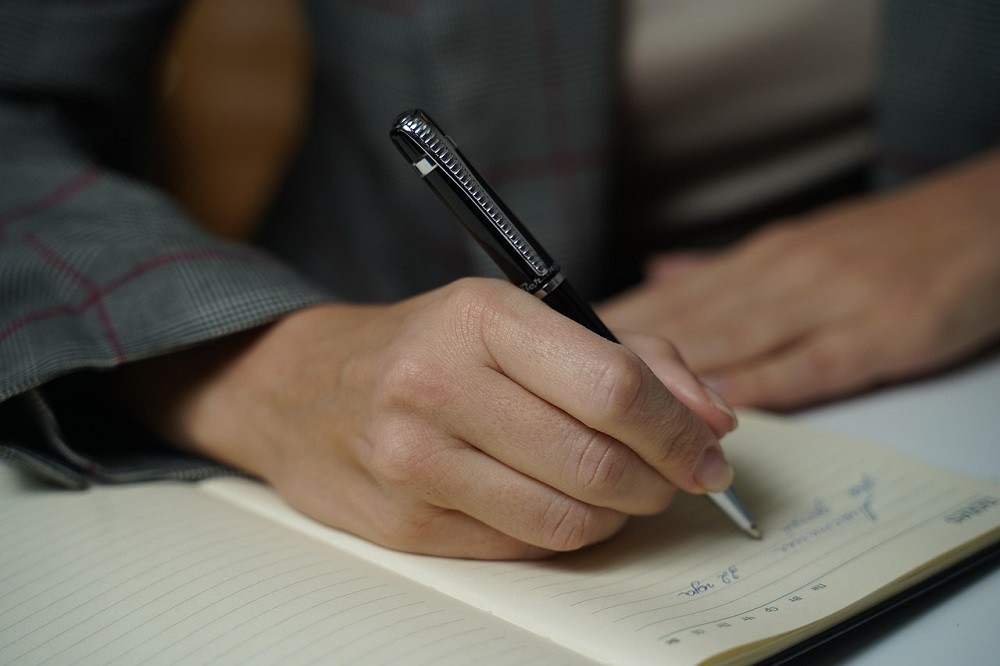 A man is writing in a journal with a pen