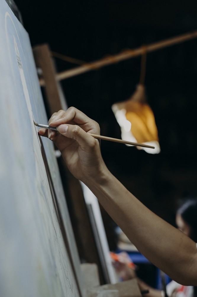 Someone is painting on a canvas. Only their arm, paintbrush, and canvas are visible