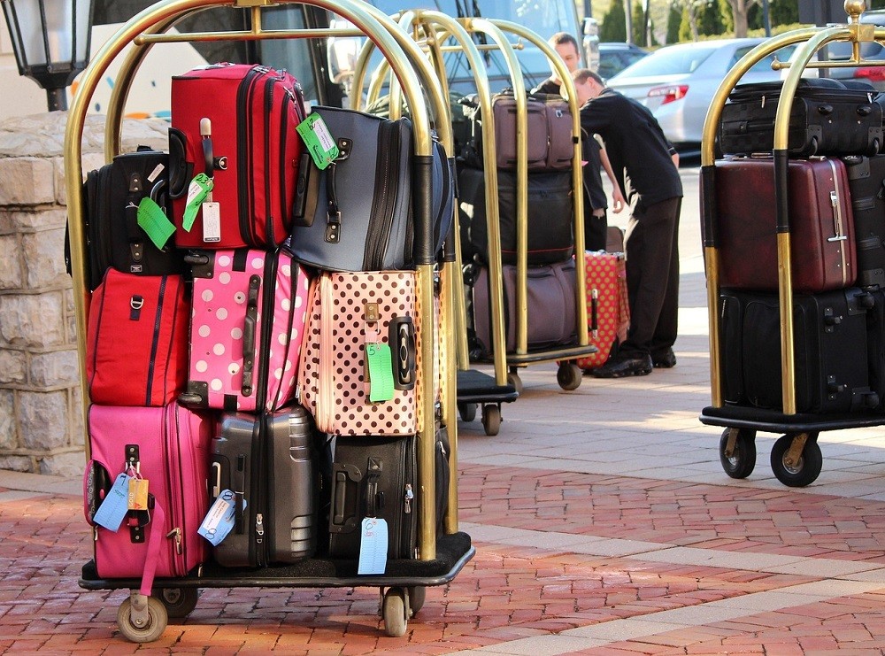 Three brass hotel luggage carts are full of luggage and bags