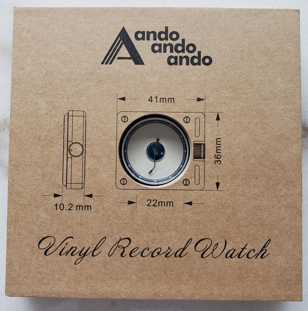 The front of the box that contains the limited edition Esteemed Gentleman Vinyl Record Watch by AndoAndoAndo. The name of the brand and brand logo is at the top, a display window features the dial of the watch including the measurements for the case. The name of the watch is at the bottom in a cursive font