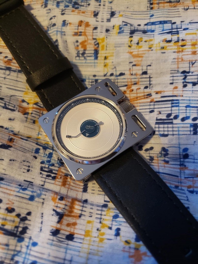 The Esteemed Gentleman vinyl record watch with white dial sits on a cloth that has music notes all over it