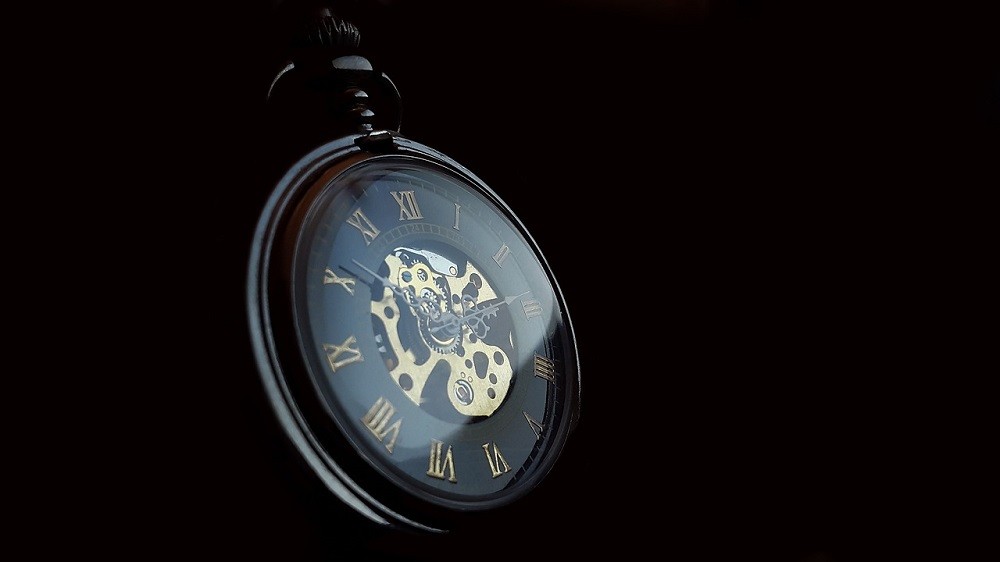 A round pocket watch sits against a black background. The middle of the watch is open and the movement is visible