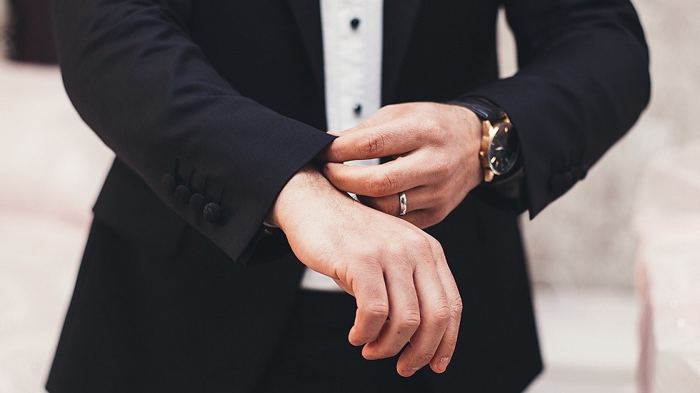 A man wearing a black suit and white dress shirt is adjusting the cuff of his jacket