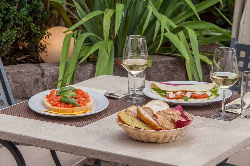 A table has plates of breads, sandwiches, and wine on it. No one is seated at the table