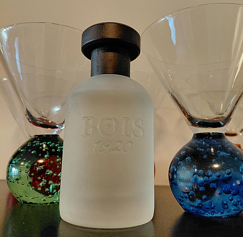 The powdered bottle of Classic 1920 cologne by Bois 1920 sits between a blue and green martini glass