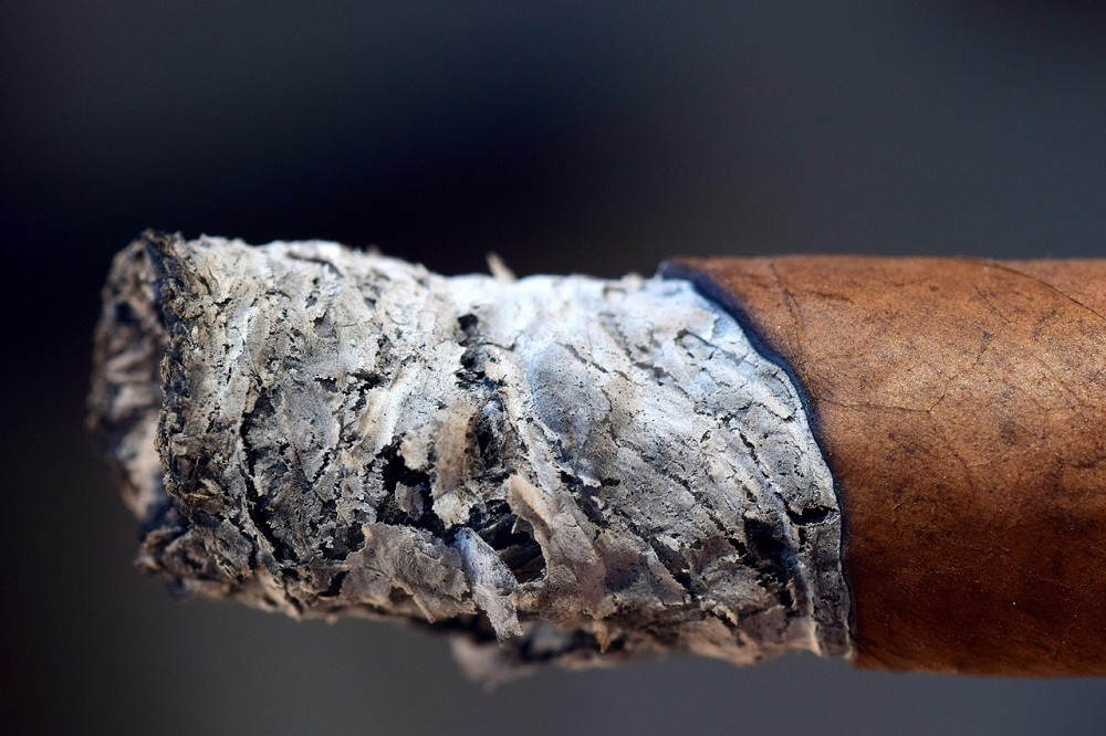 The ash of a lit cigar shows it isn't burning evenly. One side is burning faster than the other