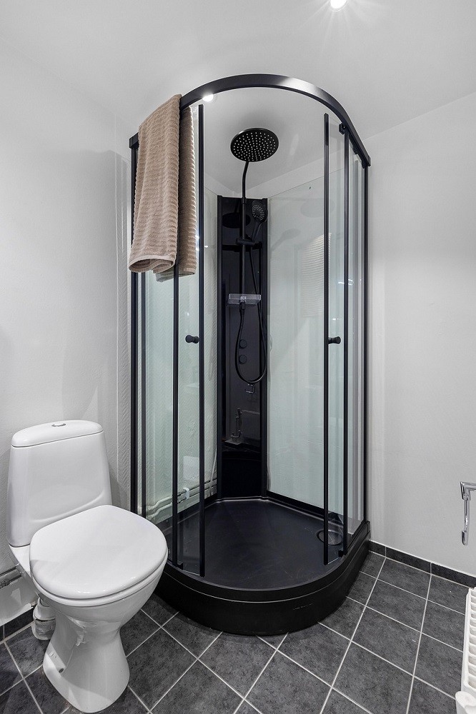 A glass shower with black faucet is in the corner of a white bathroom. There is a toilet to the left of the shower