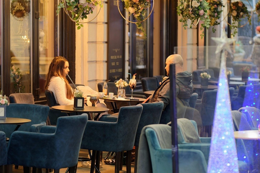 A couple is dining at a fancy restaurant. Both of them are dressed semi-formally. The woman is in a white dress and the man is wearing a grey sport jacket and black shirt