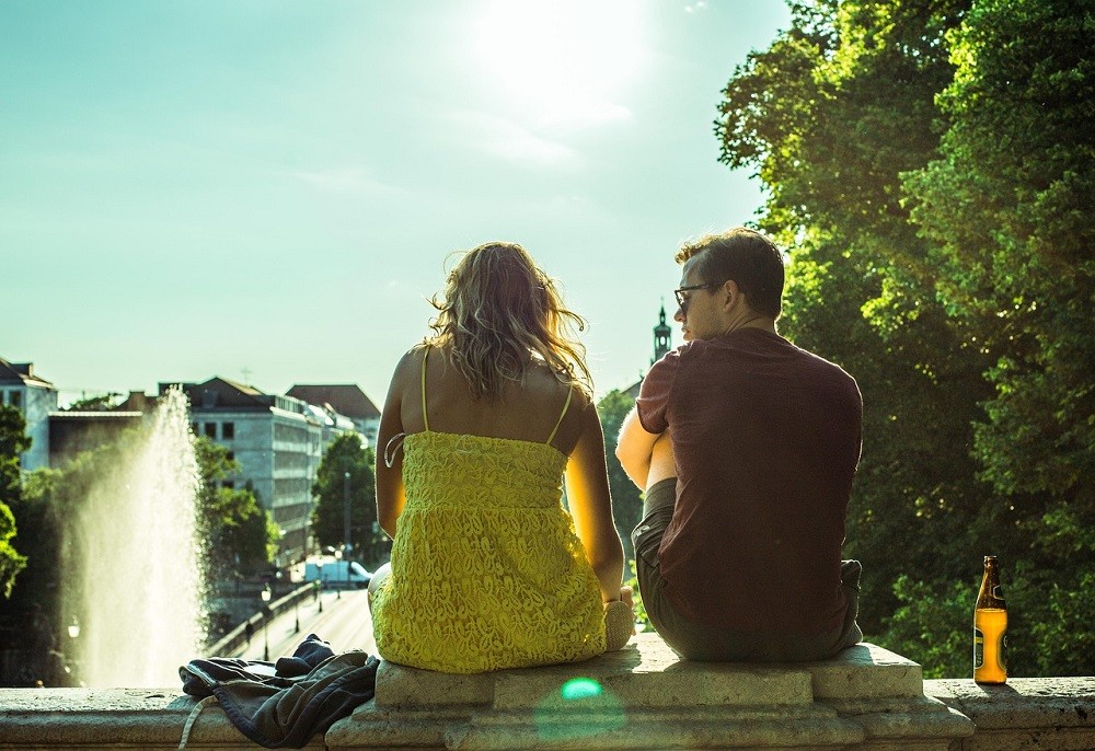 A couple sits with their back to the camera. The man (wearing a red polo shirt) is leaning in towards the woman (in a yellow dress). They are in mid conversation