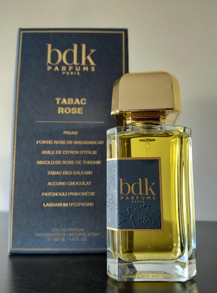 A rectangular bottle of cologne sits beside the blue and gold box it came in