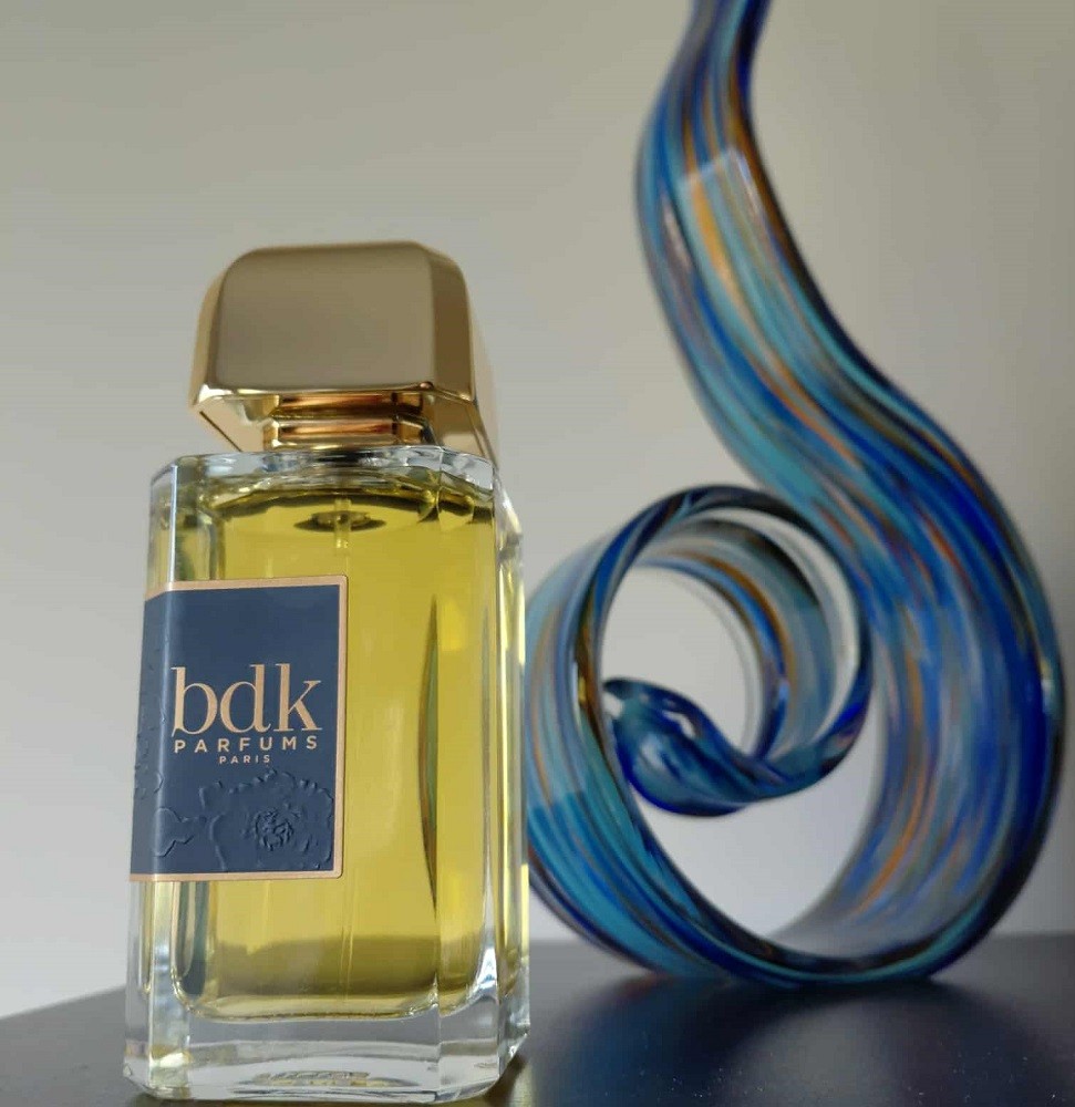A clear rectangular bottle of cologne sits beside a blue glass ornament shaped like a flame
