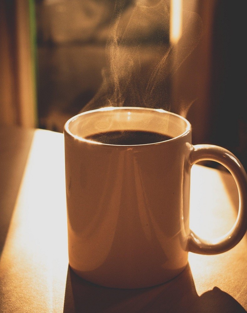 A tall, white coffee mug is full of black coffee