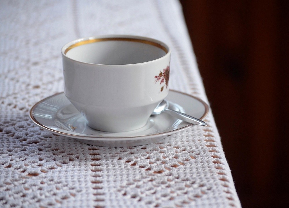 A white teacup with a gold band around the brim sits on a matching saucer with the same design