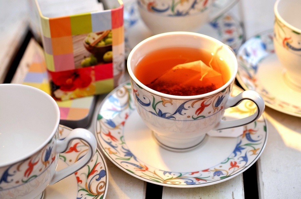 A white teacup with a rainbow floral design has a tea bag resting inside of it
