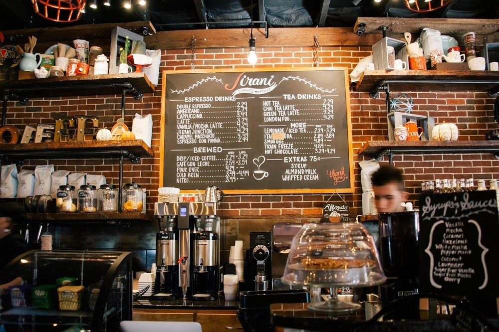 A coffee shop menu board with various coffee themed decorations and cups on shelves on each side of the board