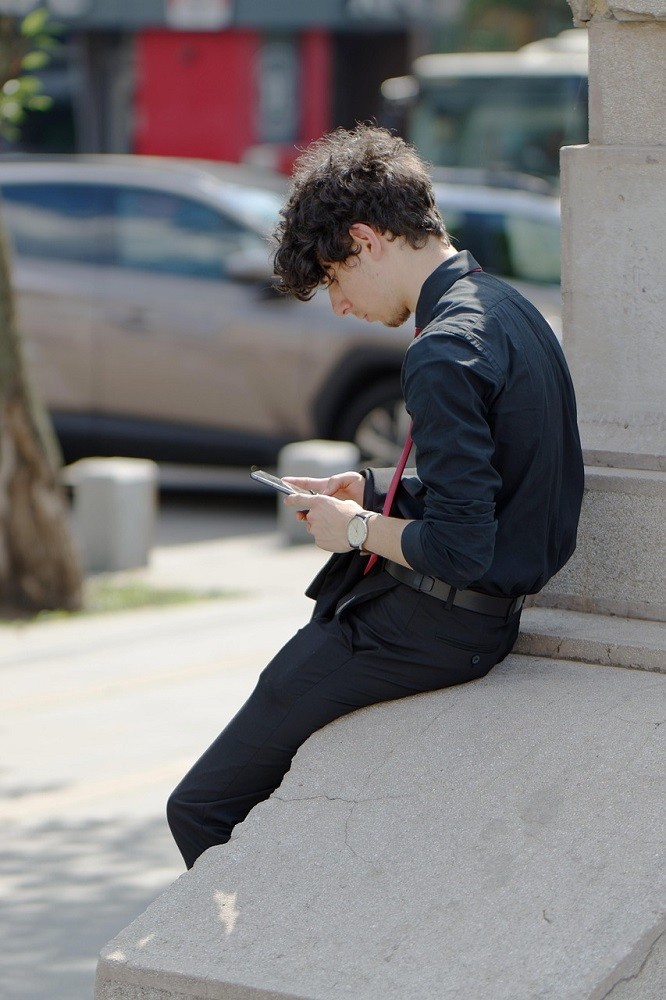 A young man sits on a step looking down at his phone