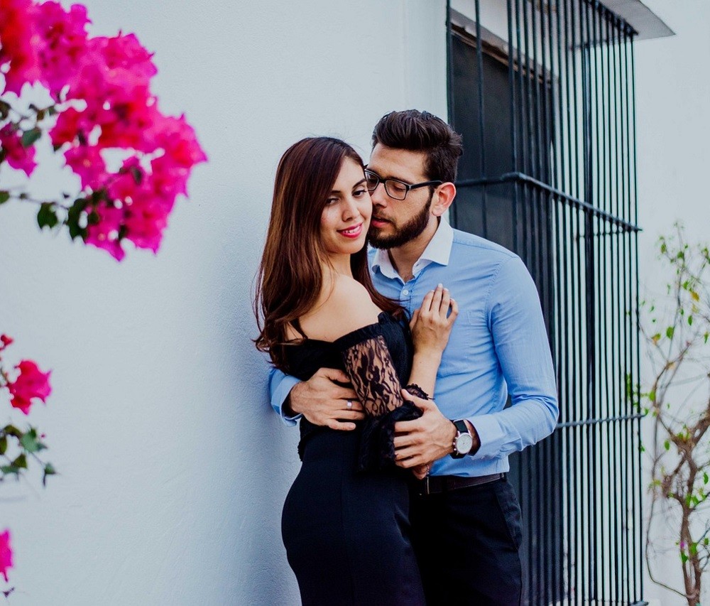 A young couple is outside a building. The man is leaning in for a kiss but the woman is pulling away