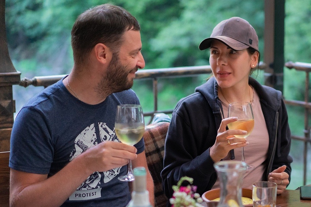 A couple sits at a table at a restaurant. They are each holding a glass of wine and having a conversation