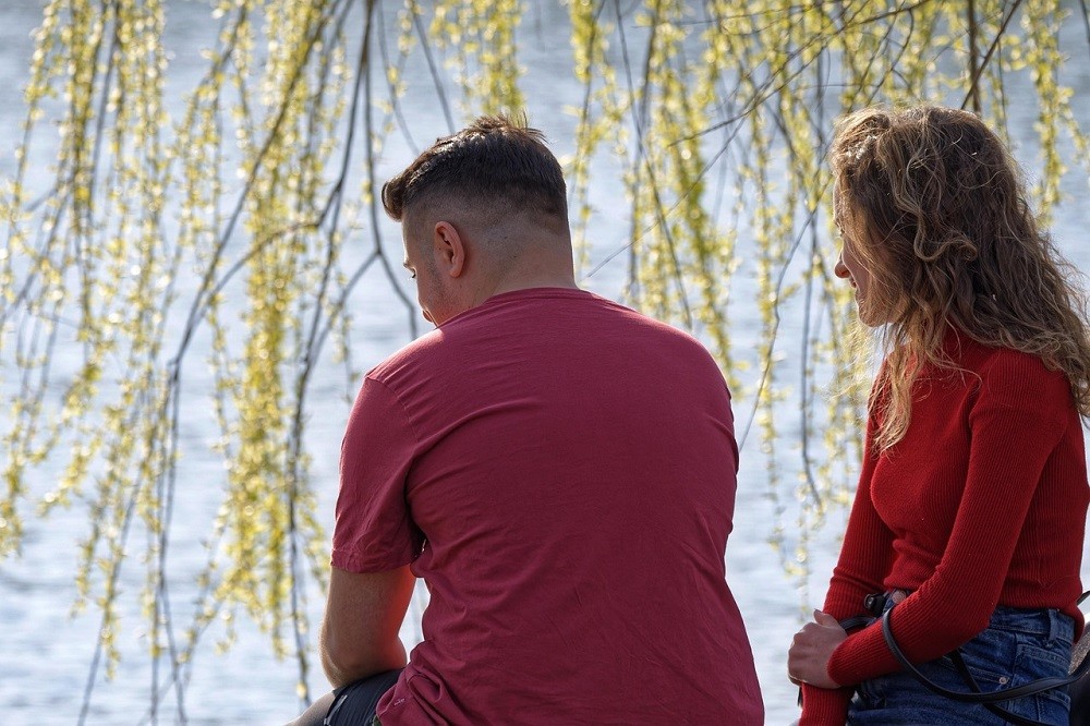 A young couple are sitting outside in the grass having a conversation