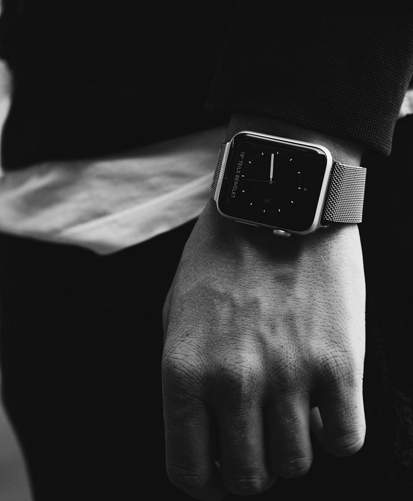 A black and white photograph of someone wearing a rectangular smart watch