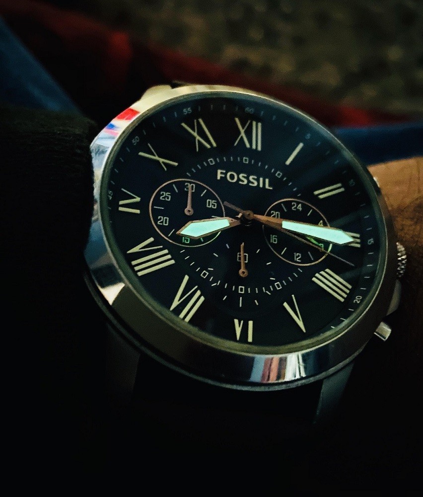 A large, black Fossil watch is shown. It is much too big for the wearers wrist