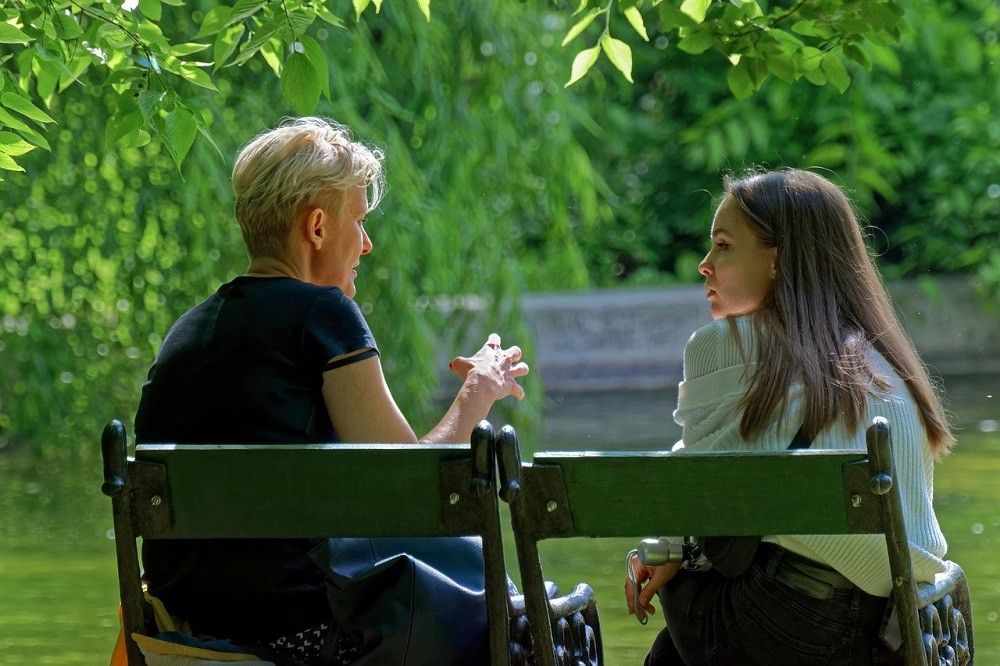 A young couple are having a conversation while sitting on a bench