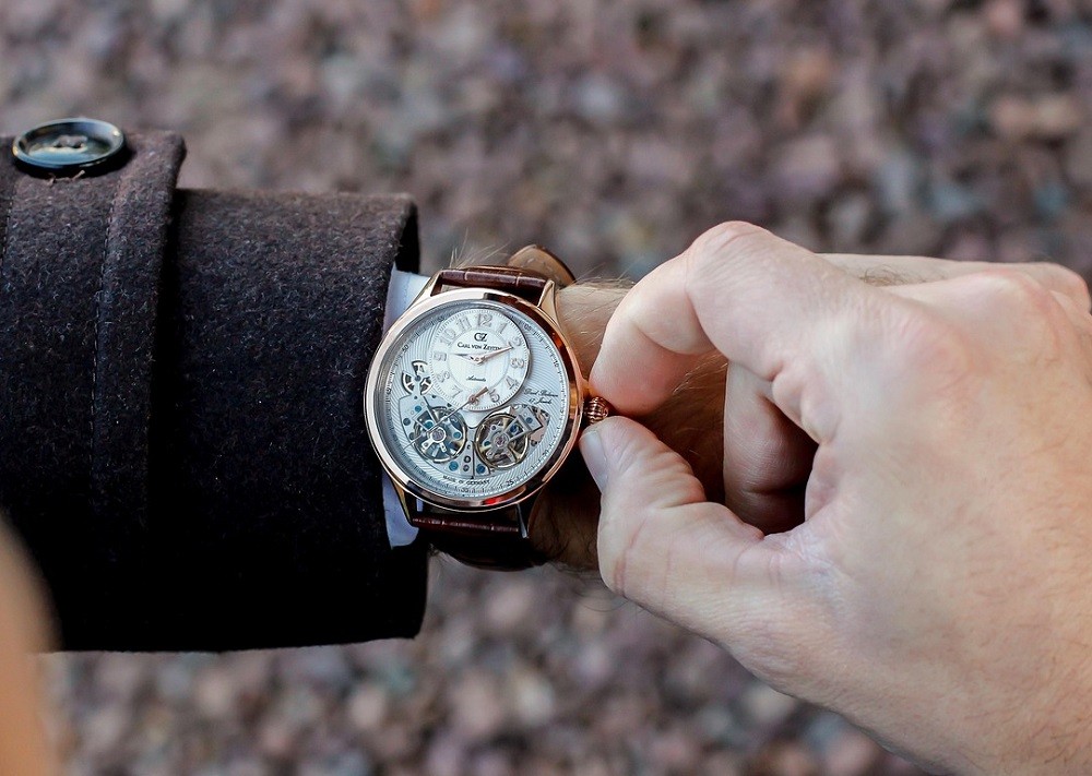 Someone is changing the time on their white-faced, gold-plated watch while it is on their wrist