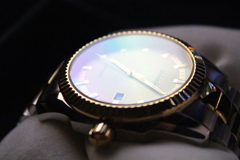 A luxury watch with a gold and silver bracelet sits on a white cushion