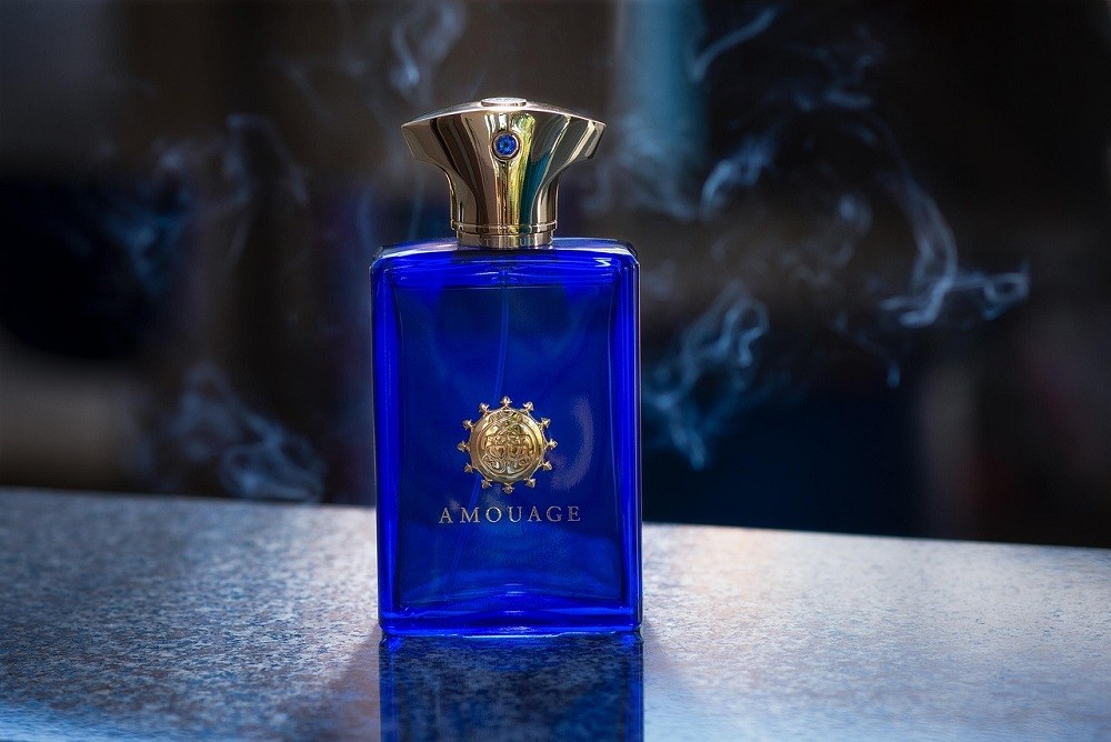 A blue, rectangular bottle of cologne with a gold cap sits on a white marble countertop