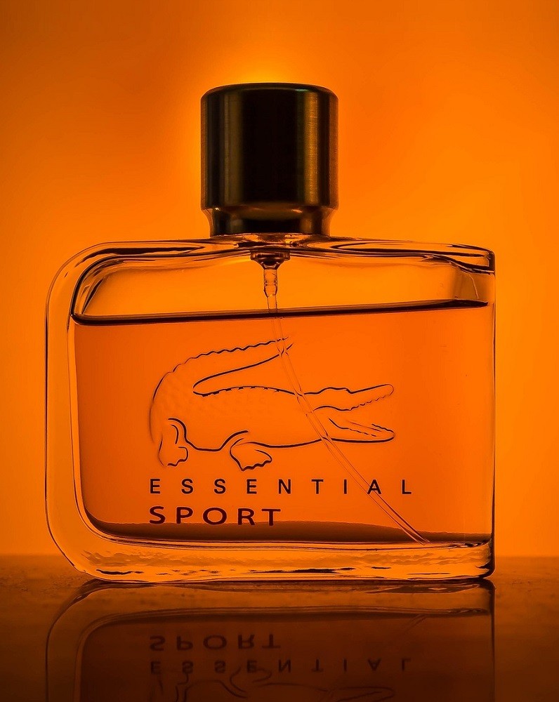 A clear, short, square bottle of cologne sits against an orange backdrop