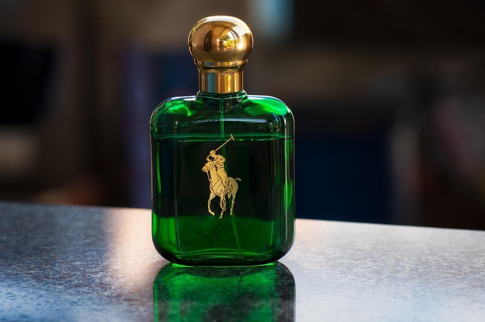 A green bottle of cologne with a gold lid sits on a black countertop