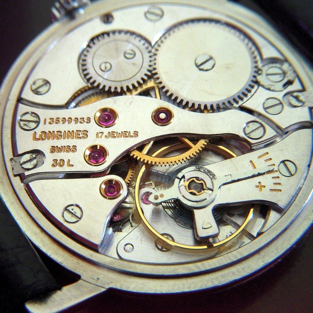 The movement from a vintage Longines wrist watch is show. The gears, levers, springs, and jewels are clearly visible