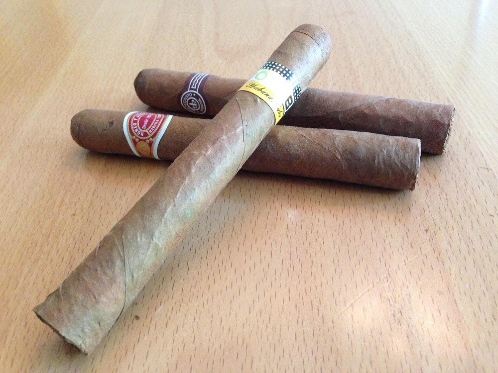 Three medium brown cigars sit on a wooden table