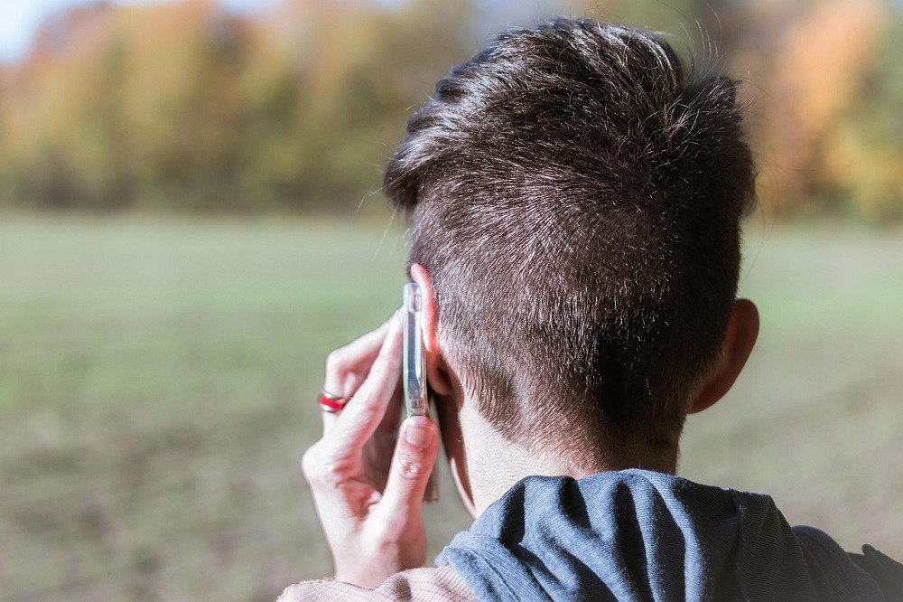 A young man holds his phone to his ear while in the middle of a conversation