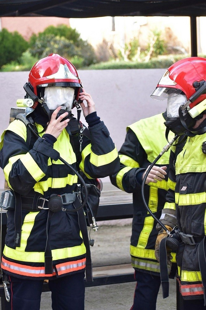 Two fire fighters are engaged in ensuring their masks fit properly