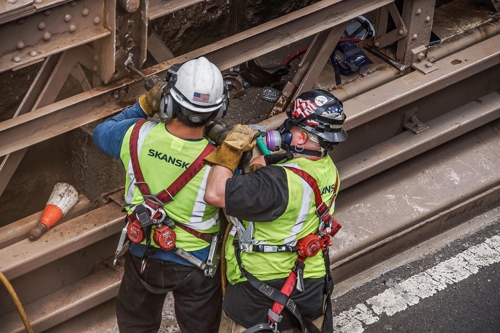 Two construction workers are working with a big drill. One is showing the other how it works