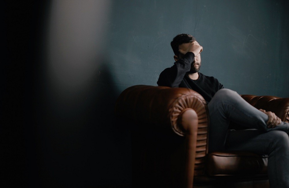 A stressed man sits in a leather chair with his hands over his face