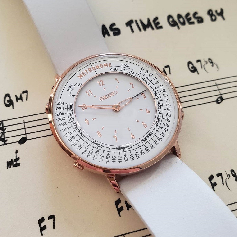A white variant of the Seiko metonome watch with gold case is laying on a piece of sheet music