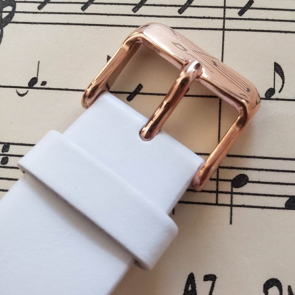 The gold buckle of the Seiko Metronome watch is showcased. It is attached to a white leather strap