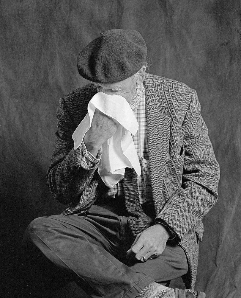 An elderly man blows his nose in to a large handkerchief