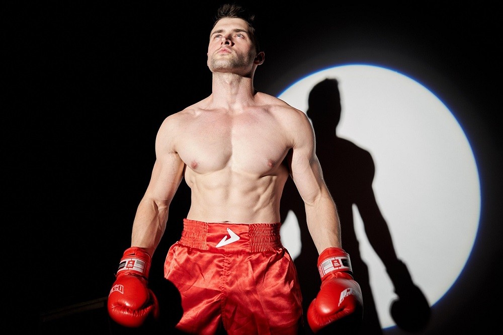 A boxer in red shorts stands proud in front of a bright spotlight