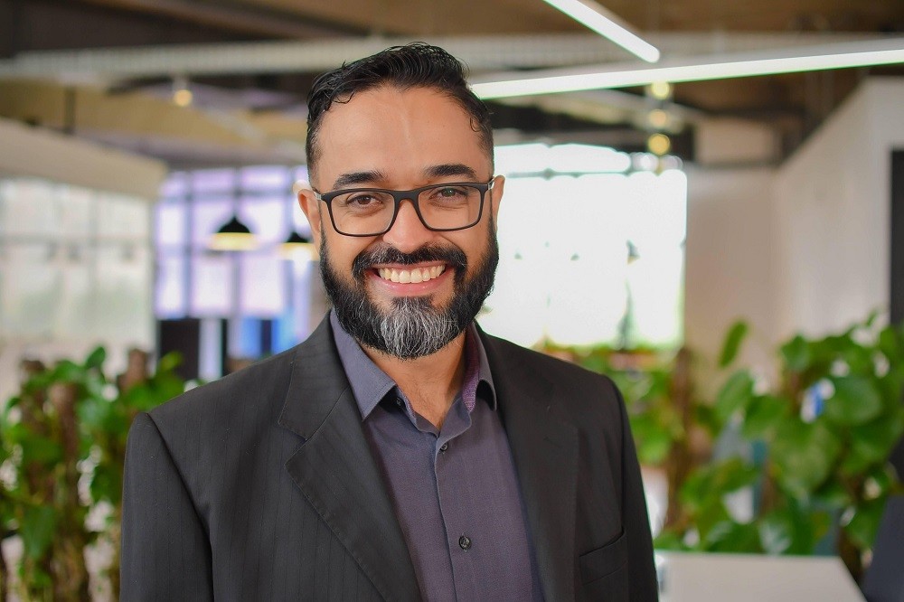 A businessman wearing a suit with a black beard and black glasses is smiling